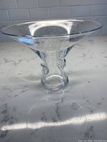 Clear flared glass vase with sculpted glass details near the base, shown from an angle.