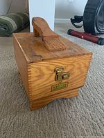 Photo of the vintage Griffin Shinemaster wooden shoeshine box with handle on top and brass latch, sitting on carpet.