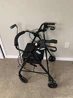 Black walker with padded seat, basket, and three wheels for mobility.