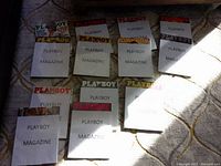 Lot of 13 vintage Playboy magazines laid out with covers partially obscured by paper sheets labeled 'PLAYBOY MAGAZINE'.