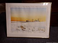 Framed print showing the full artwork depicting a snowy rural landscape at sunset with buildings and a coyote.