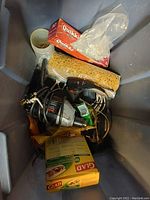 Top down view inside tote showing mixed items: power drill, large sponge, disposable gloves box, screws in a plastic cup, and cling wrap box.