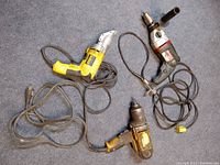Three corded power tools on carpet: DeWalt metal shears, DeWalt impact wrench, Metabo hammer drill.
