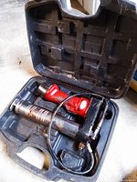 Electric grease gun with attached flexible hose and grease cartridge inside the black carrying case.
