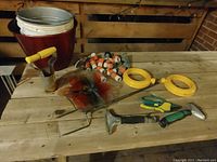 Photo of garden accessories on wooden surface including buckets, hand tools, hose connectors, hose guide stakes, and wind spinner.