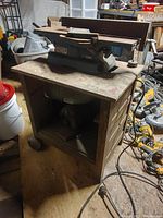 Photo of the jointer placed on top of the wooden cabinet showing the full assembly and surrounding workshop area with tools on the floor.