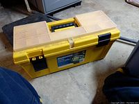 Photo of large yellow Mastercraft toolbox on concrete floor, showing top and one side with label and latches.