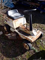 Front-left angle view of the white lawn tractor showing black seat and rusted body.