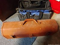Top view of two items: an orange metal tool box and blue and black fabric tool bag, placed next to each other on a carpeted floor.