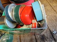 Box containing a collection of vintage kitchen items including a light blue kitchen scale, multiple metal tins, a red scoop, and a Cerito small box.
