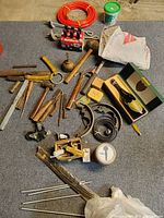 Overview of all tools and miscellaneous items laid out on carpet, including hand tools, wooden mallet, cast iron parts, red tubing, and boxed ceramic bell.