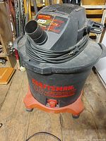 Front and side view of Craftsman 10 gallon shop vacuum with power cord wrapped around top motor housing. Orange base and black cylindrical body. Missing hose attachment on front suction port.