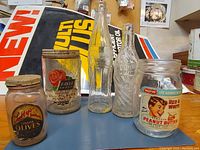 Five vintage glass bottles and jars arranged on a blue surface with labels visible, showing a variety of saved food and condiment containers.