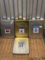 Four Walt Disney Treasures DVD collectible metal tins in silver, bronze, and gold colors placed on a woven surface.