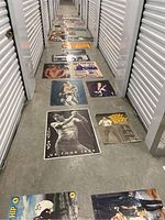 Long hallway view of multiple vintage rock posters laid on the floor showing band images including Iggy Pop and The Tragically Hip.