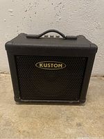 Front view of the amplifier showing black metal grille with Kustom logo and black textured vinyl casing.