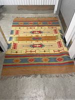 Full view of flatweave rug laid on concrete floor, showing overall pattern, color bands and fringe at ends