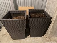 Two large brown wicker pattern outdoor garden planters side by side with soil and some leaf debris inside.
