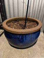 Blue garden pot with soil and a plant stand inserted, viewed from above at an angle.
