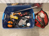 Blue plastic crate containing various tools and hardware items mixed together, with a red tool bag beside it.