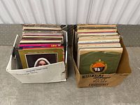 Two cardboard boxes filled with vinyl records showing album covers and record labels, some with visible wear.