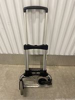 Folded view of the hand truck showing telescoping handle and compact design with wheels visible.