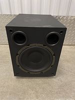 Front view of a black Proficient powered subwoofer showing the speaker driver and two front bass ports.