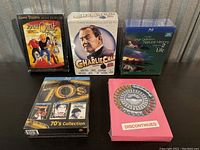 Five sealed DVD collections displayed on a dark surface, including Johnny Yuma, Charlie Chan, High Definition Natural History Life Volume 2, 70's Collection, and Discontinued with birth control pill artwork.