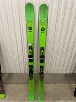 Full view of a pair of green Rossignol Smash 7 skis with bindings attached standing upright.