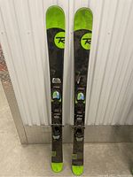 Full view of the pair of Rossignol Smash 7 skis showing black and lime green color with bindings attached.
