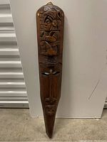 Full view of the tall wooden tribal mask carved with face and figure.