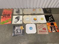Overview of eleven vinyl records and sleeves arranged on floor showing variety of album covers and paper sleeves.