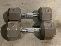 Two 20 lb gray hex dumbbells on concrete floor showing both dumbbells side by side and their metal knurled textured handles.