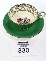 Aynsley green teacup and saucer displayed with auction lot number showing floral interior and gold leaf border.