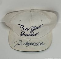 Front shot showing white baseball cap with New York Yankees embroidery and Jim Catfish Hunter autograph on the brim.