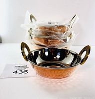 Four stacked La Coppera bowls, front one unwrapped showing hammered copper exterior and ornate handles