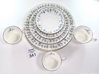 Set of four stacks showing three sizes of plates and three matching teacups with blue floral and gold pattern.