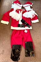 Red Santa jacket, pants, two Santa hats, three black belts and black boot gators laid out on floor