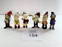 Front view of six vintage Christmas elf/gnome figurines in varied colorful clothing and Christmas-themed poses with hanging hooks, showing used condition.