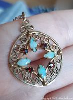 Closeup of pendant showing four turquoise-colored marquise-shaped stones and four round red stones set in gold filigree.