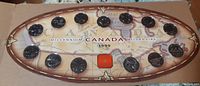 Oval wooden display box containing 15 Canadian millennium quarters from 1999, arranged in a map outline of Canada, labeled 'Millennium CANADA 1999'.