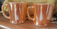 Two vintage Anchor Hocking orange luminescent mugs placed side by side showing glossy finish and handle shape.
