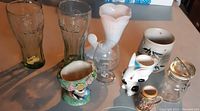 Overview of assorted collectibles and receptacles including Coca-Cola glasses, milk glass vase, ceramic pieces, and glass jar