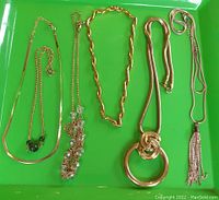 Six gold toned necklaces displayed on green background showing chain styles and pendants