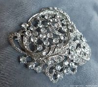 Close-up photo showing the detailed rhinestone arrangement and silver-tone filigree metal base of the pin.