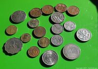 Photo showing 18 international coins arranged on a green surface, varied in size, shape, and metal tone.