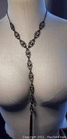 Front view of the long black floral-design necklace displayed on a dress form, showing the Y-shaped dangling design with rhinestone accents.
