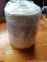 Cone of white wool yarn wrapped in plastic, showing full size and shape of yarn cone.