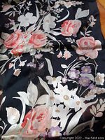 Close-up of the floral pattern on the scarf showing pink roses, white flowers, and leaves on black background.