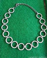 Full view of the rhinestone necklace showing circular links and adjustable chain against a green background.